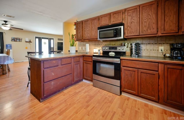 kitchen featuring kitchen peninsula, stainless steel appliances, light wood-type flooring, and backsplash