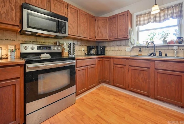 kitchen with tasteful backsplash, sink, light hardwood / wood-style floors, stainless steel appliances, and decorative light fixtures