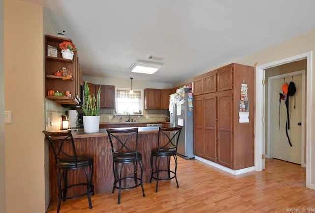 kitchen featuring a breakfast bar area, kitchen peninsula, backsplash, stainless steel fridge with ice dispenser, and light wood-type flooring