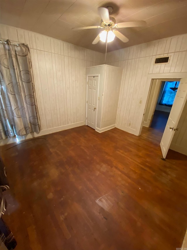 spare room with ceiling fan, wood-type flooring, and wooden walls