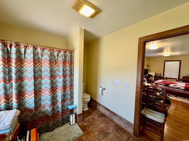 bathroom with a textured ceiling, toilet, and tile patterned flooring