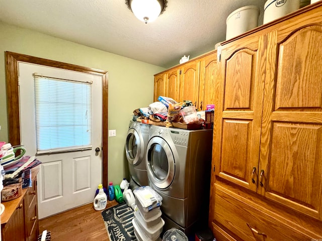 washroom with a textured ceiling, washing machine and dryer, light wood-type flooring, and cabinets