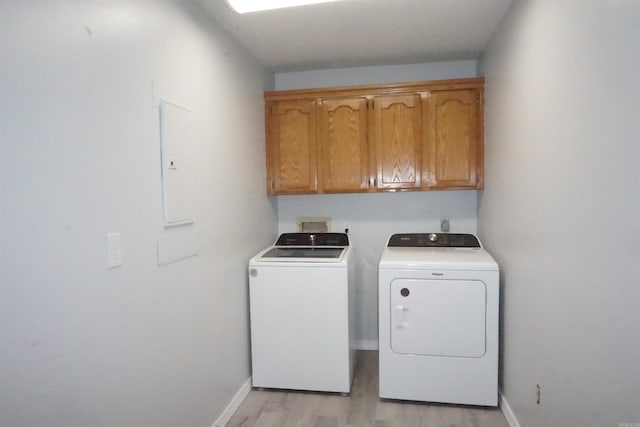 clothes washing area featuring cabinets, electric panel, washing machine and dryer, and light hardwood / wood-style floors