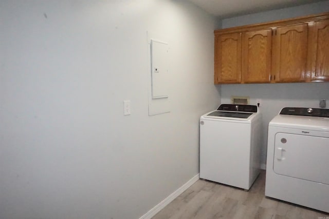 clothes washing area featuring electric panel, washer and clothes dryer, light hardwood / wood-style floors, and cabinets