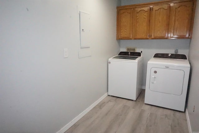 washroom featuring washer and dryer, electric panel, cabinets, and light wood-type flooring