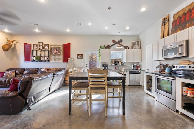 kitchen featuring white cabinets, stainless steel appliances, concrete flooring, and decorative light fixtures