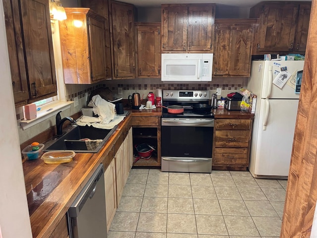 kitchen featuring wooden counters, sink, light tile patterned floors, appliances with stainless steel finishes, and tasteful backsplash