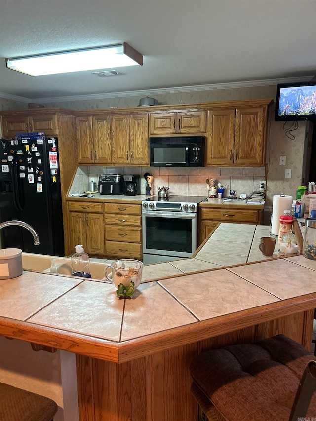 kitchen featuring a breakfast bar area, tile counters, black appliances, and crown molding