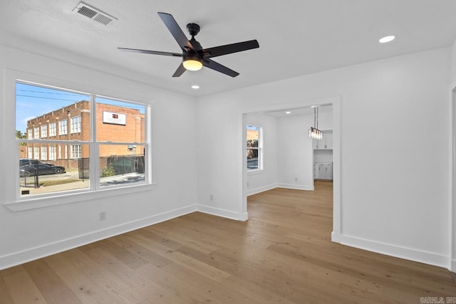 spare room featuring plenty of natural light, ceiling fan with notable chandelier, and hardwood / wood-style floors