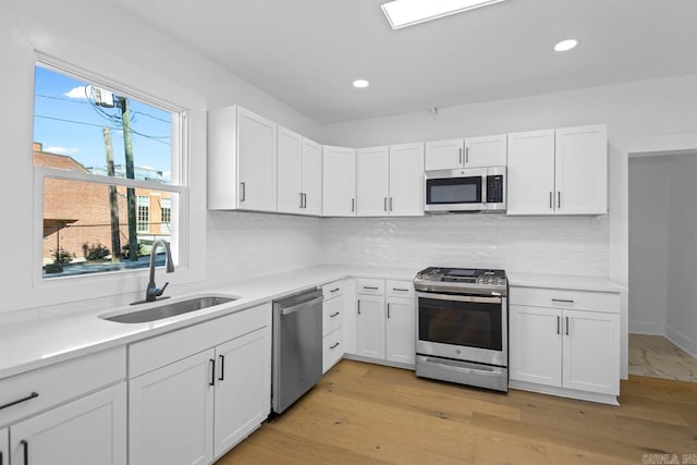 kitchen with sink, appliances with stainless steel finishes, light hardwood / wood-style flooring, and white cabinetry