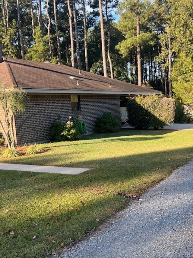 view of side of home with a lawn, a shingled roof, and brick siding