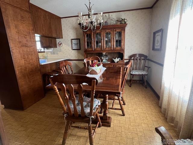 dining space with wallpapered walls, crown molding, and a notable chandelier