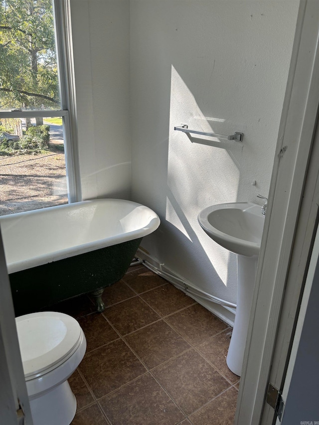 bathroom featuring toilet, a tub to relax in, and tile patterned floors