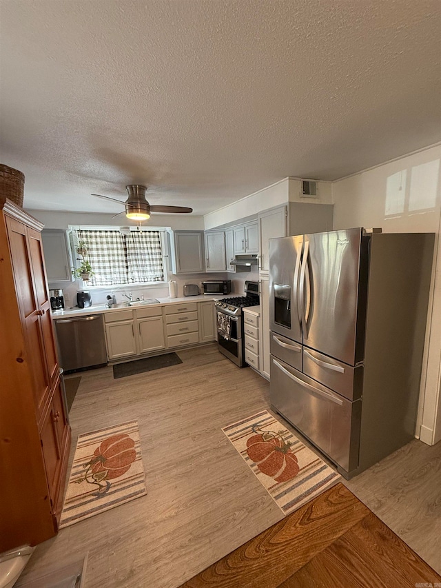 kitchen featuring stainless steel appliances, sink, light wood-type flooring, a textured ceiling, and ceiling fan