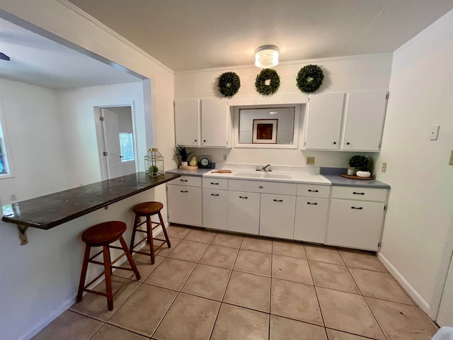 kitchen featuring ornamental molding, a kitchen breakfast bar, white cabinetry, and light tile patterned floors