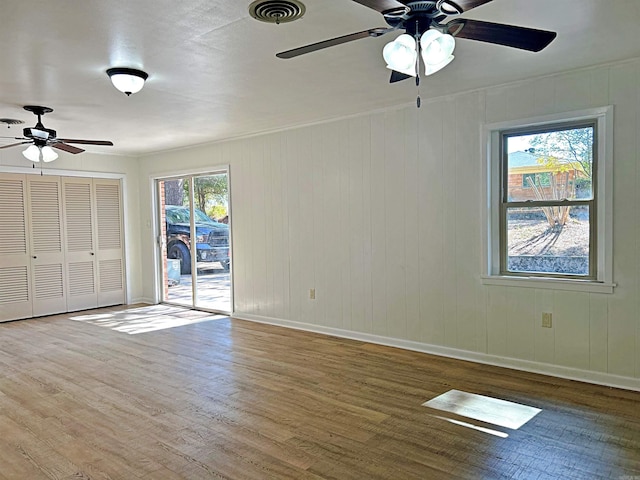 empty room with ceiling fan, a wealth of natural light, and hardwood / wood-style floors