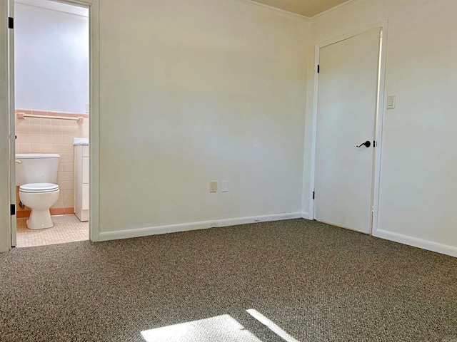 unfurnished bedroom with tile walls, connected bathroom, and carpet floors