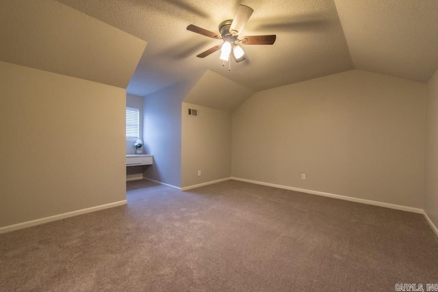 bonus room with lofted ceiling, a textured ceiling, dark carpet, and ceiling fan