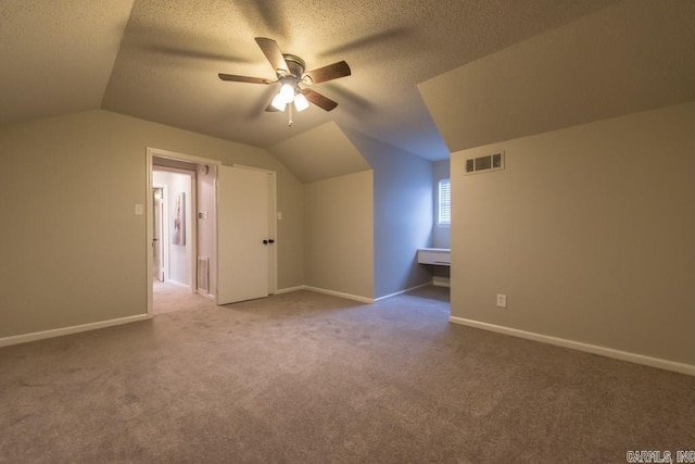 additional living space with carpet, vaulted ceiling, a textured ceiling, and ceiling fan