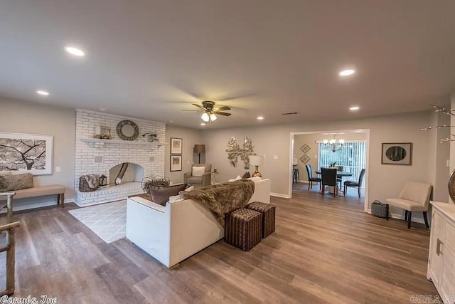 living room featuring dark wood-type flooring, a fireplace, and ceiling fan with notable chandelier