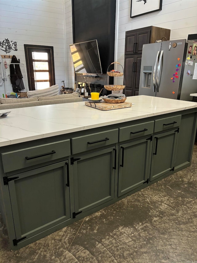 kitchen with light stone countertops, green cabinets, wooden walls, and stainless steel refrigerator with ice dispenser