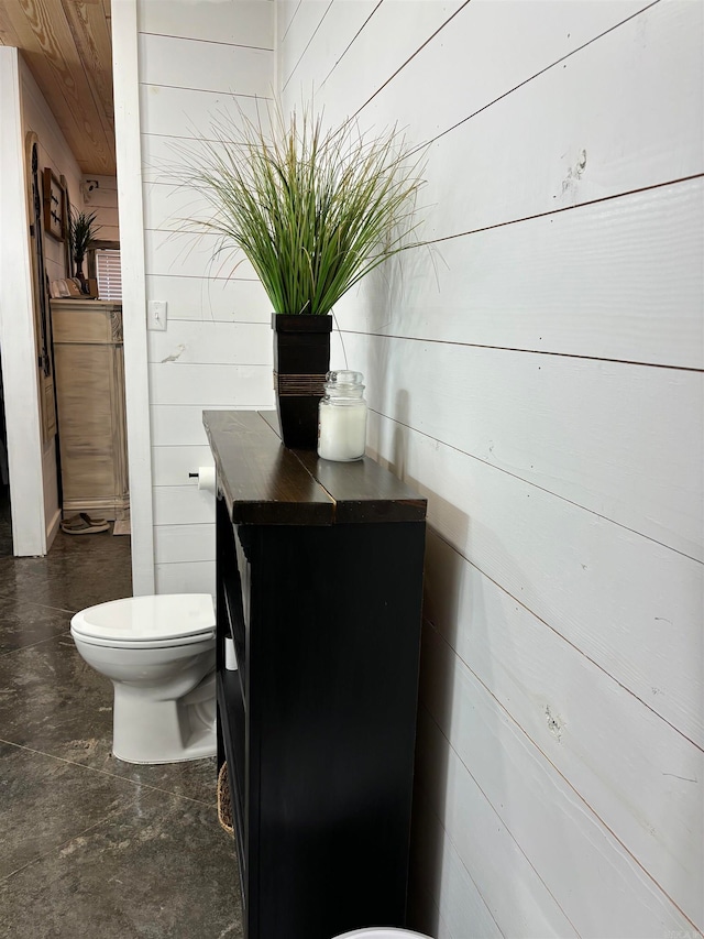 bathroom featuring concrete floors, vanity, wooden walls, and toilet