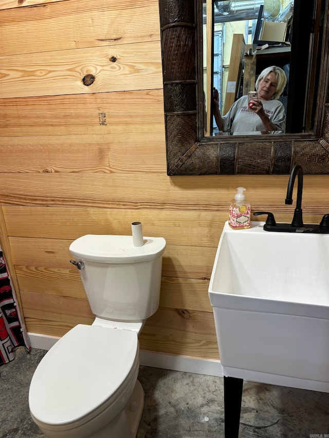 bathroom featuring toilet, wood walls, and sink