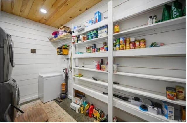 laundry room with stacked washer / drying machine, laundry area, wooden ceiling, and wood walls