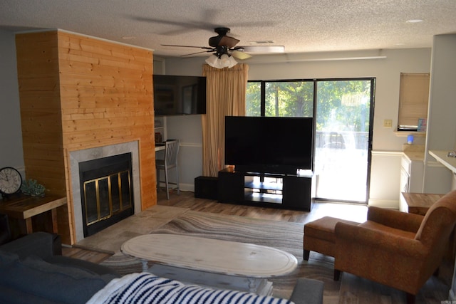 living room featuring ceiling fan, a tiled fireplace, a textured ceiling, and hardwood / wood-style floors