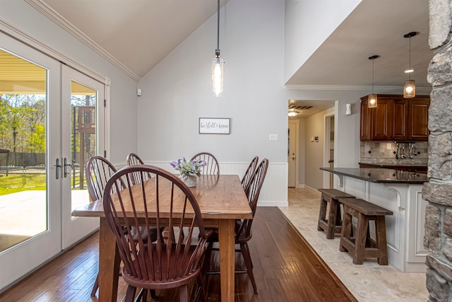 dining room featuring french doors, light hardwood / wood-style floors, high vaulted ceiling, and ornamental molding