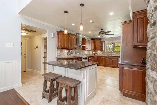 kitchen with wall chimney range hood, hanging light fixtures, ceiling fan, a breakfast bar, and dark stone countertops