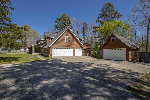 view of front facade featuring roof with shingles, an outbuilding, a detached garage, fence, and a front yard