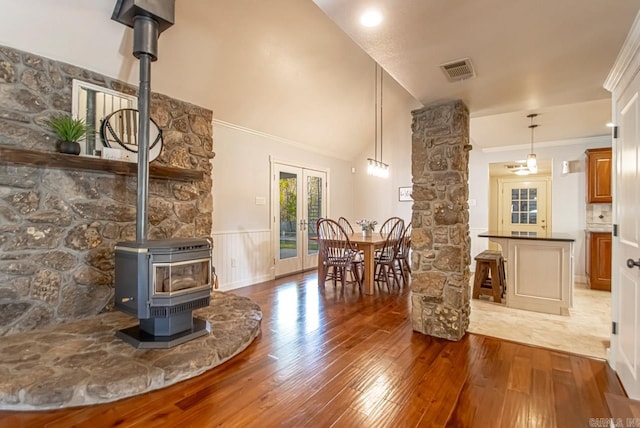 interior space with pendant lighting, hardwood / wood-style floors, high vaulted ceiling, and a wood stove