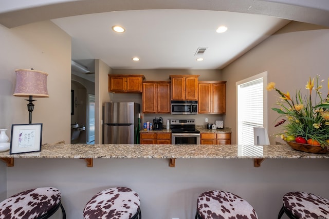 kitchen with appliances with stainless steel finishes, kitchen peninsula, light stone counters, and a kitchen breakfast bar