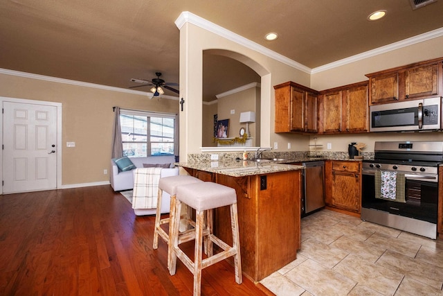 kitchen with a kitchen breakfast bar, light hardwood / wood-style flooring, kitchen peninsula, stainless steel appliances, and ornamental molding