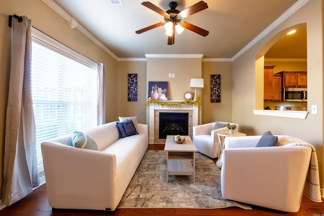 living room featuring a tiled fireplace, crown molding, hardwood / wood-style flooring, and ceiling fan