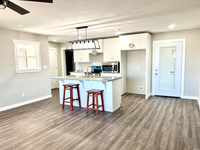 kitchen with a kitchen island with sink, dark wood-type flooring, pendant lighting, stone counters, and white cabinetry