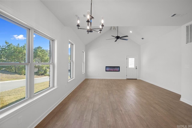 unfurnished living room featuring a wealth of natural light, hardwood / wood-style floors, vaulted ceiling, and ceiling fan with notable chandelier