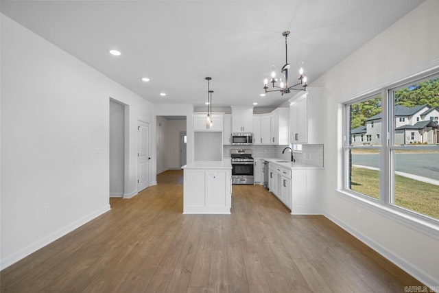 kitchen with light hardwood / wood-style flooring, hanging light fixtures, stainless steel appliances, a center island, and white cabinetry