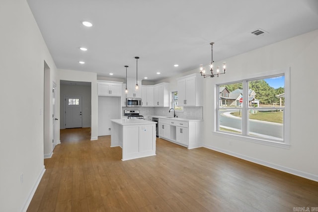 kitchen featuring appliances with stainless steel finishes, a kitchen island, white cabinetry, and hanging light fixtures