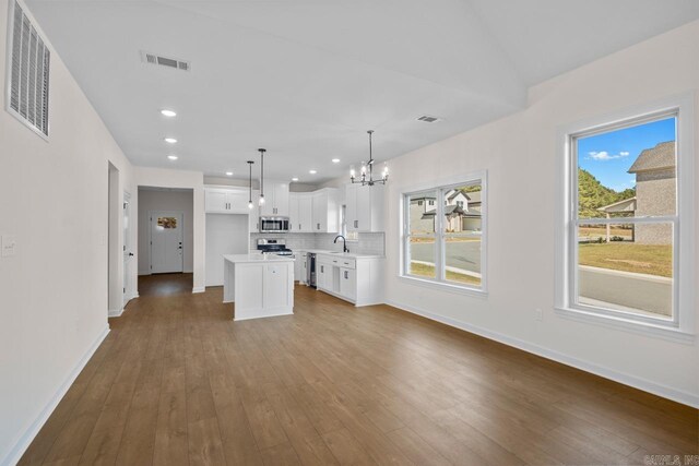 kitchen with appliances with stainless steel finishes, a kitchen island, white cabinetry, pendant lighting, and light hardwood / wood-style flooring