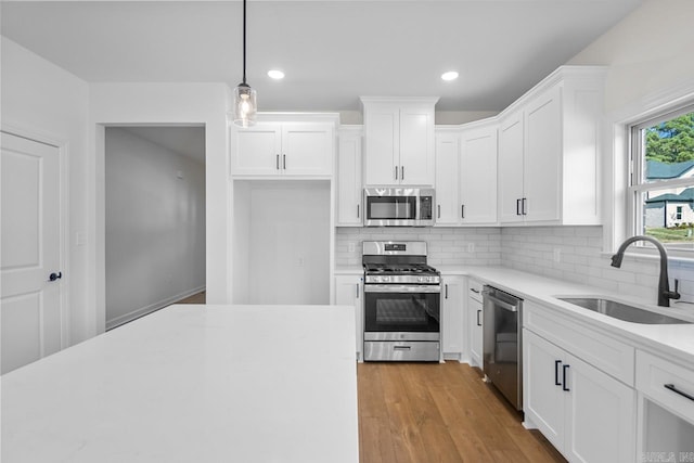 kitchen with sink, light hardwood / wood-style floors, stainless steel appliances, decorative light fixtures, and white cabinets