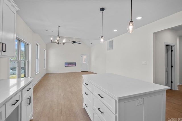 kitchen with lofted ceiling, hanging light fixtures, a center island, white cabinetry, and light hardwood / wood-style floors