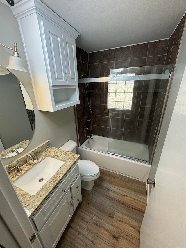 full bathroom with wood-type flooring, a textured ceiling, toilet, enclosed tub / shower combo, and vanity