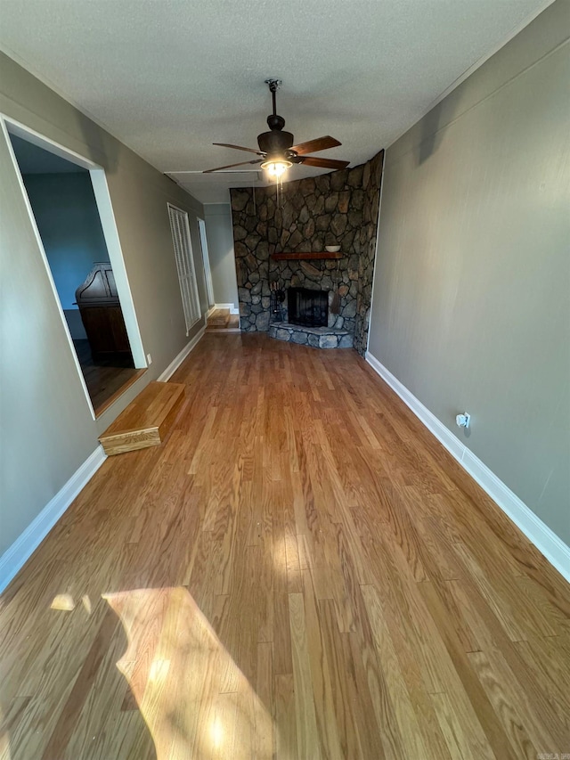 unfurnished living room with light hardwood / wood-style floors, a textured ceiling, a stone fireplace, and ceiling fan