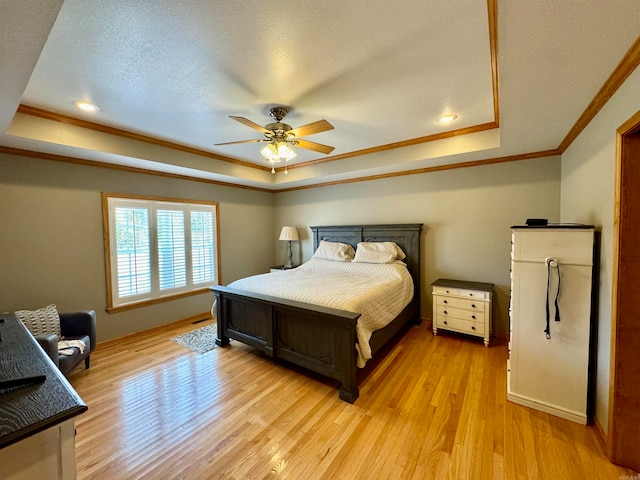 bedroom featuring ceiling fan, a textured ceiling, a tray ceiling, ornamental molding, and light hardwood / wood-style floors