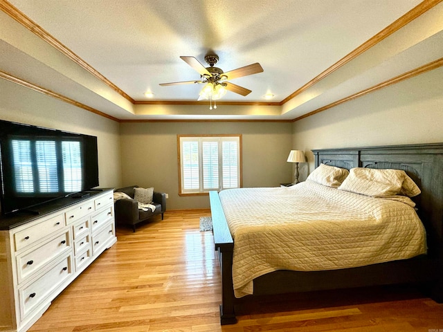 bedroom with light wood-type flooring, a textured ceiling, a tray ceiling, ceiling fan, and crown molding