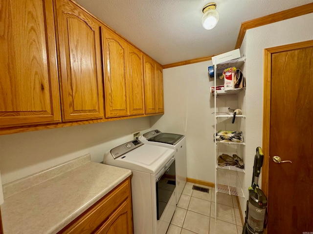 clothes washing area featuring crown molding, light tile patterned floors, washing machine and dryer, a textured ceiling, and cabinets