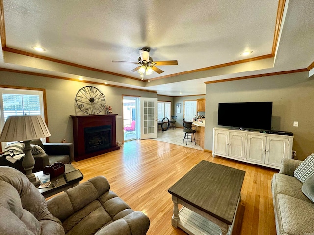 living room with light hardwood / wood-style flooring, ornamental molding, ceiling fan, and a raised ceiling