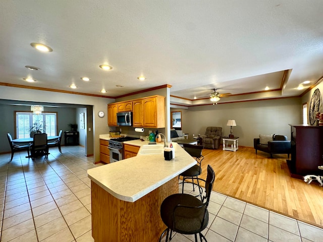 kitchen with kitchen peninsula, stainless steel appliances, ornamental molding, sink, and light wood-type flooring